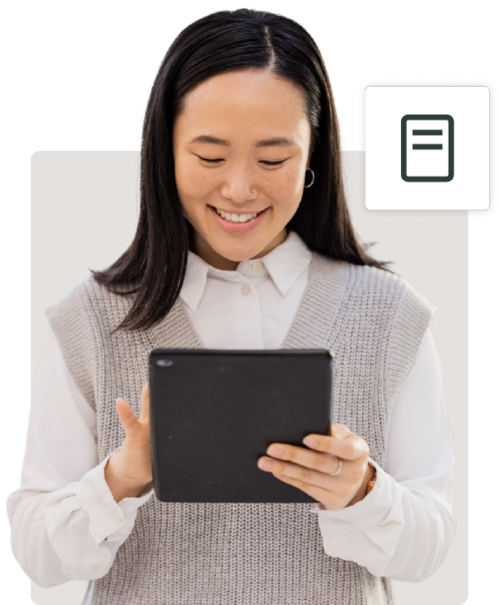 A young asian woman smiling, looking at a tablet she's holding with both hands, dressed in a white shirt and gray sweater vest, isolated on a white background.